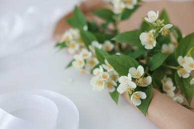 Photo of Jasmine branches and kraft paper on white table, closeup. Space for text