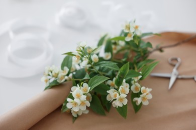 Photo of Jasmine branches, scissors and kraft paper on white table, closeup