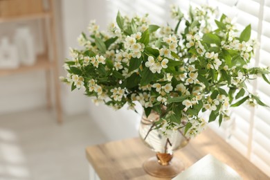 Photo of Bouquet of beautiful jasmine flowers in vase on wooden table indoors