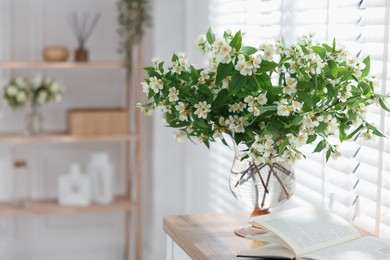 Photo of Bouquet of beautiful jasmine flowers in vase on wooden table indoors. Space for text