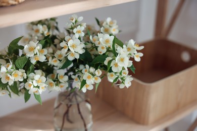 Photo of Bouquet of beautiful jasmine flowers in vase on shelving unit indoors, closeup