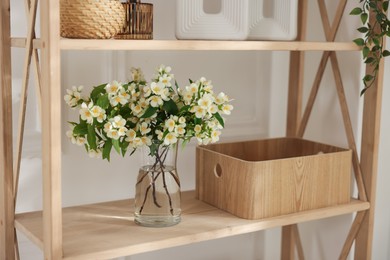 Photo of Bouquet of beautiful jasmine flowers in vase on shelving unit indoors