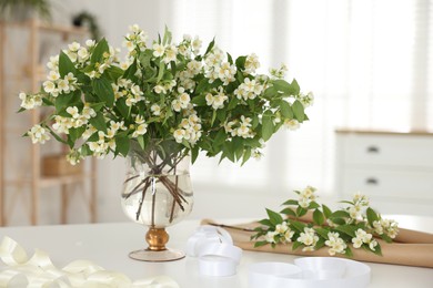 Photo of Bouquet of beautiful jasmine flowers in vase on white table indoors