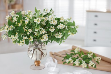 Photo of Bouquet of beautiful jasmine flowers in vase on white table indoors