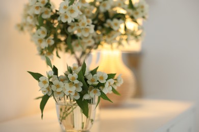 Photo of Bouquet of beautiful jasmine flowers in vase on white table indoors, closeup. Space for text