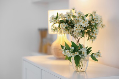 Photo of Bouquet of beautiful jasmine flowers in vase on white table indoors. Space for text