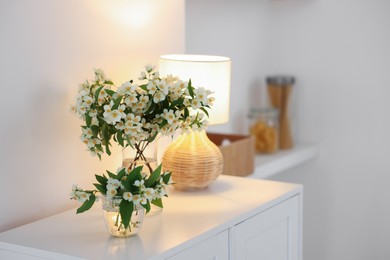 Photo of Bouquet of beautiful jasmine flowers in vase on white table indoors. Space for text