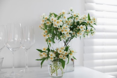 Photo of Bouquet of beautiful jasmine flowers in vase on white table indoors