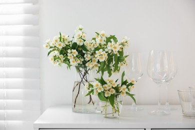 Photo of Bouquet of beautiful jasmine flowers in vase on white table indoors