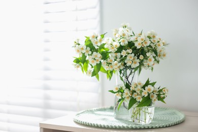 Photo of Bouquet of beautiful jasmine flowers in vase on table indoors. Space for text