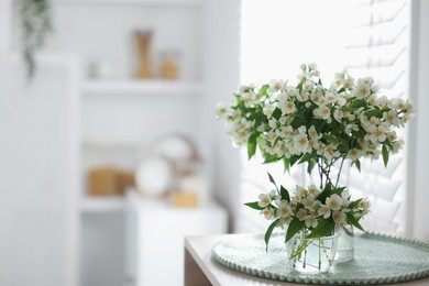 Photo of Bouquet of beautiful jasmine flowers in vase on table indoors. Space for text