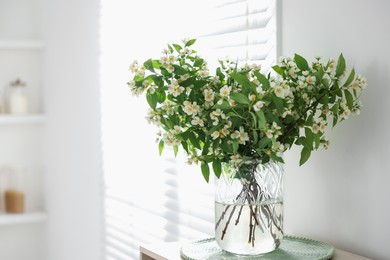 Photo of Bouquet of beautiful jasmine flowers in vase on table indoors. Space for text