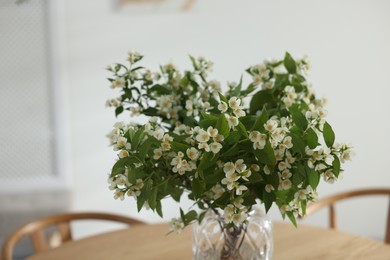 Photo of Bouquet of beautiful jasmine flowers in vase on wooden table indoors, closeup