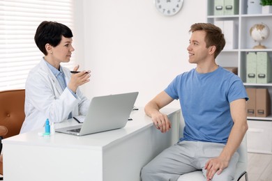 Photo of Ophthalmologist consulting young man at white table in clinic