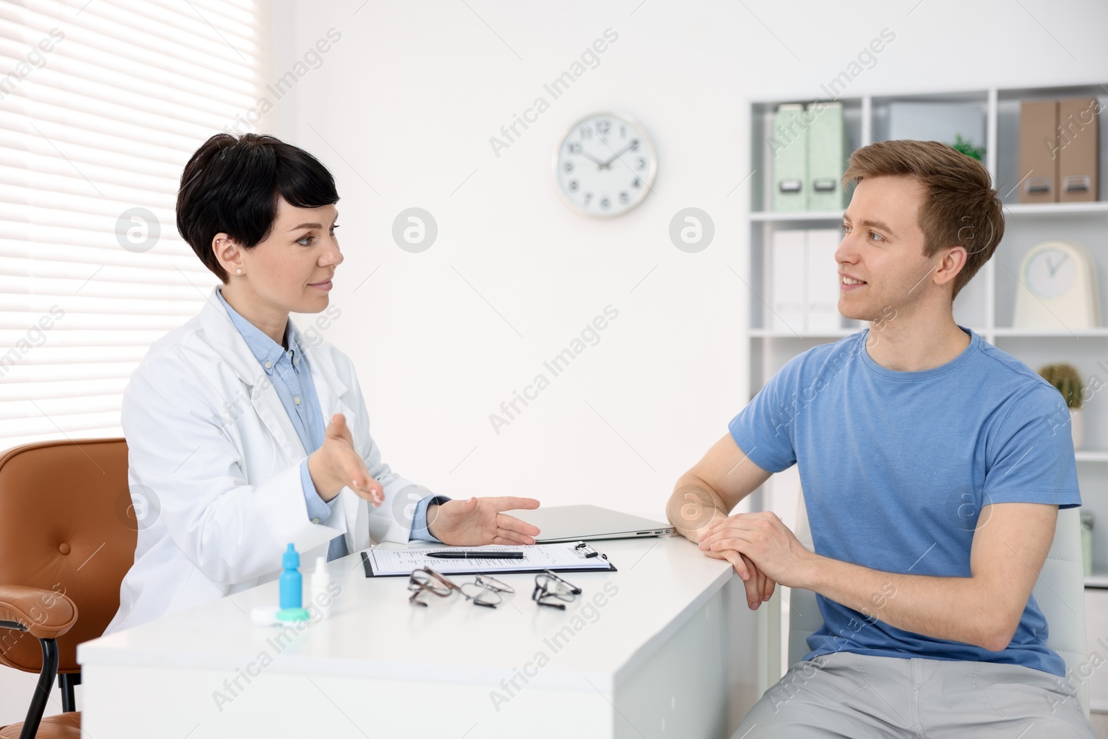 Ophthalmologist consulting young man at white table in clinic Photo of Ophthalmologist consulting young man at white table in clinic