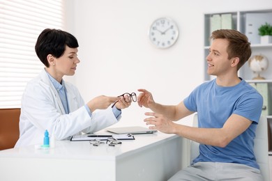 Photo of Ophthalmologist giving glasses to patient at white table in clinic