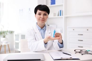 Photo of Portrait of professional ophthalmologist with eye drops at white table in clinic