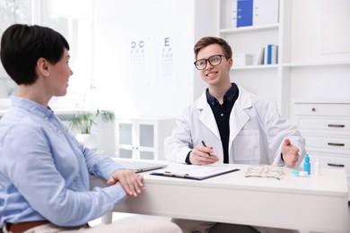 Photo of Ophthalmologist consulting woman at white table in clinic