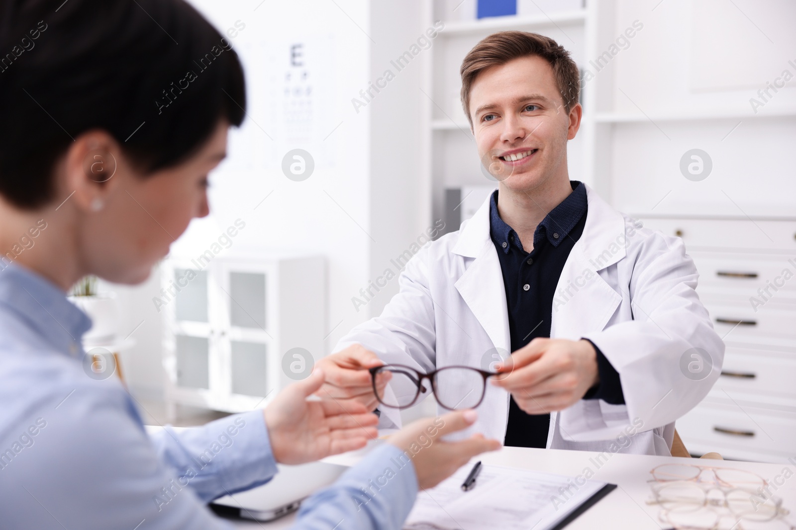 Ophthalmologist giving glasses to patient at white table in clinic Photo of Ophthalmologist giving glasses to patient at white table in clinic