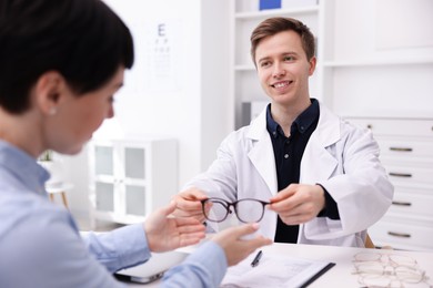 Photo of Ophthalmologist giving glasses to patient at white table in clinic