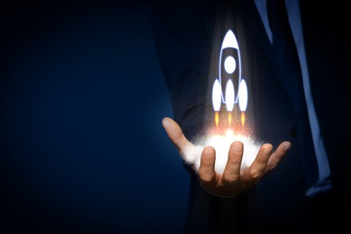 Image of Business, successful startup. Man holding virtual rocket on against dark blue background, closeup