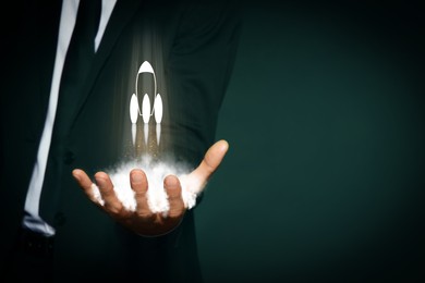 Image of Business, successful startup. Man holding virtual rocket on against dark green background, closeup