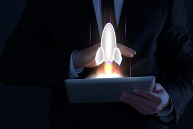Image of Business, successful startup. Man using tablet computer against dark background, closeup. Rocket launching from device