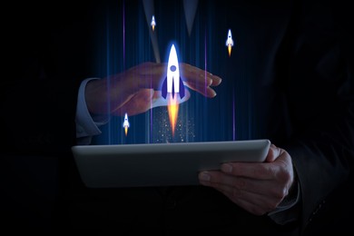 Image of Business, successful startup. Man using tablet computer against dark background, closeup. Rocket launching from device