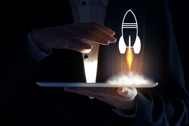 Image of Business, successful startup. Man using tablet computer against dark background, closeup. Rocket launching from device