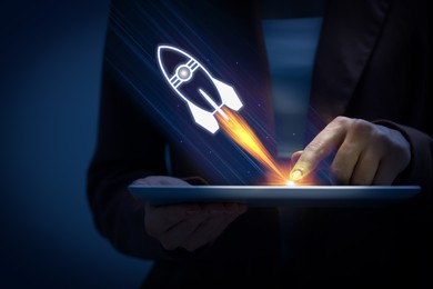 Image of Business, successful startup. Woman using tablet computer against dark background, closeup. Rocket launching from device