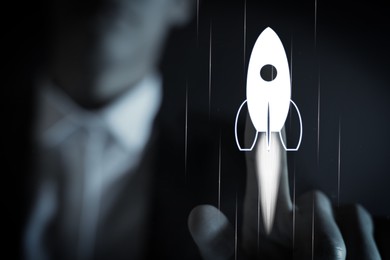 Image of Business, successful startup. Man launching rocket on virtual screen against dark background, closeup
