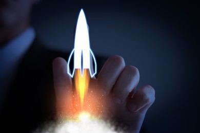 Image of Business, successful startup. Man launching rocket on virtual screen against dark blue background, closeup