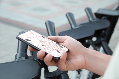 Image of Man looking at city map on his mobile phone while taking electric kick scooter outdoors, closeup
