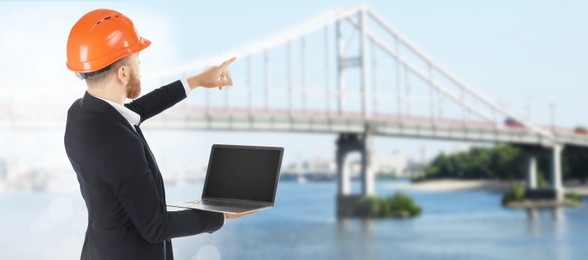 Image of Construction engineer with laptop pointing at bridge outdoors. Banner design