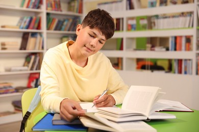 Photo of Student with books studying at table in library