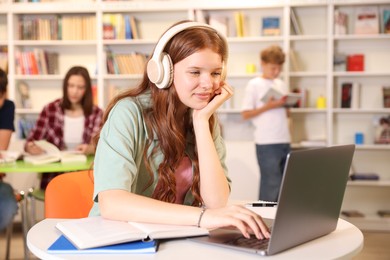 Photo of Student with laptop studying at table in library