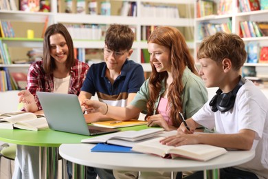 Photo of Students with books and laptop studying together at table in library