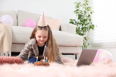 Photo of Birthday celebration. Little girl with cake having video call via laptop at home