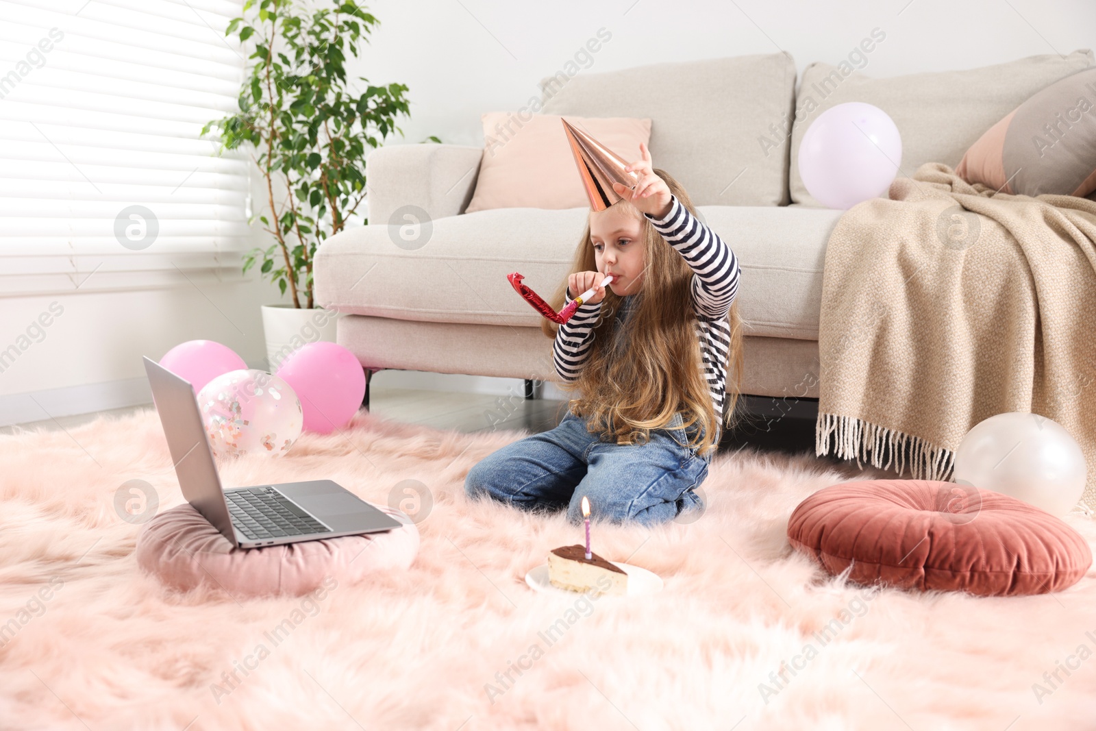 Birthday celebration. Little girl with blower and piece of cake having video call via laptop at home Photo of Birthday celebration. Little girl with blower and piece of cake having video call via laptop at home