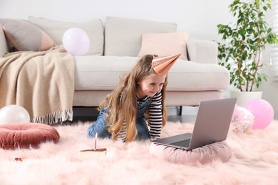 Photo of Birthday celebration. Little girl with piece of cake having video call via laptop at home
