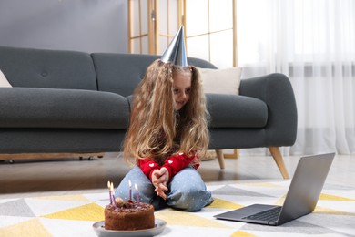 Photo of Birthday celebration. Little girl with cake having video call via laptop at home