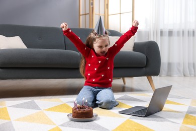 Photo of Birthday celebration. Little girl with cake having video call via laptop at home
