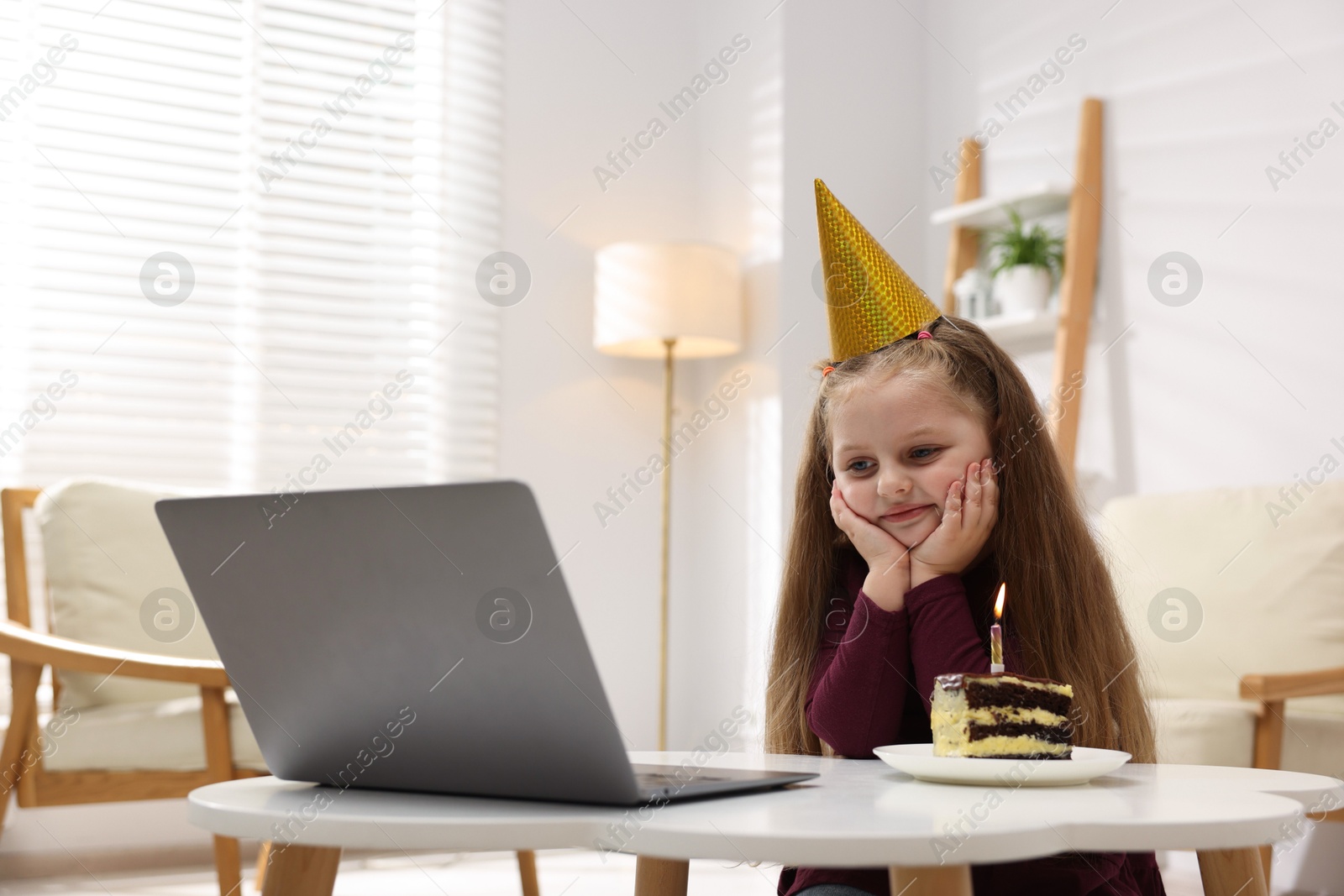 Birthday celebration. Little girl with piece of cake having video call via laptop at table indoors Photo of Birthday celebration. Little girl with piece of cake having video call via laptop at table indoors