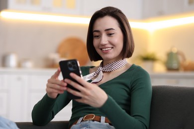 Photo of Woman using modern smartphone on sofa at home