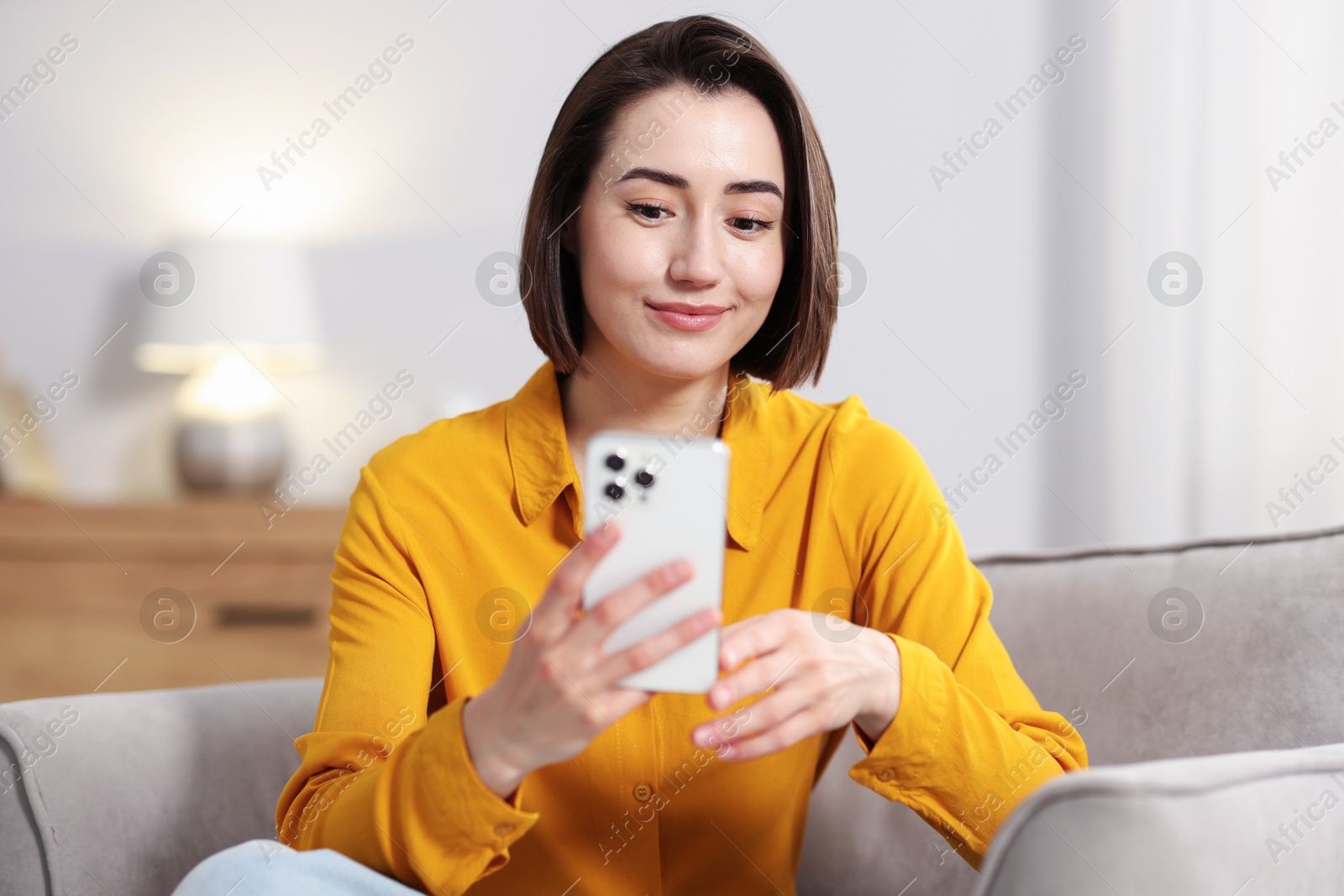 Woman using modern smartphone in armchair at home Photo of Woman using modern smartphone in armchair at home
