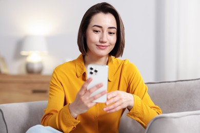 Photo of Woman using modern smartphone in armchair at home