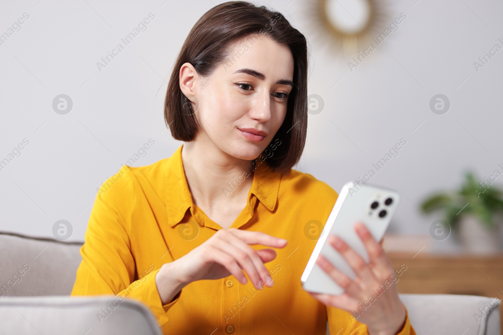 Woman using modern smartphone in armchair at home Photo of Woman using modern smartphone in armchair at home