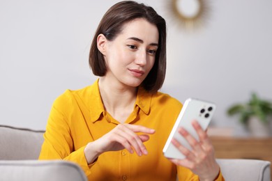 Photo of Woman using modern smartphone in armchair at home