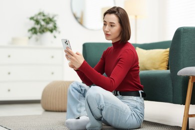 Photo of Woman using modern smartphone on floor at home