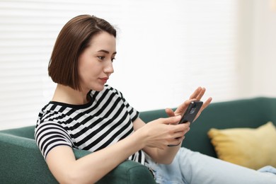 Photo of Woman using modern smartphone on sofa at home. Space for text